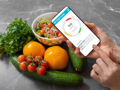 healthy food on table with hands in the foreground holding a phone with personalized nutrition app