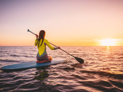 photo of woman paddle boarding in ocean at sunset; summer fitness ideas concept