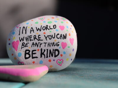 photo of a painted rock that says "In a world where you can be anything be kind."