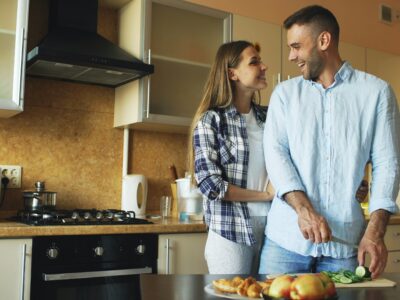 Happy young couple embracing and talking in the kitchen while cooking together at home