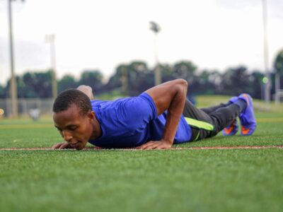 man in blue tank top lying on green grass field during daytime working out with rebuild your base fitness