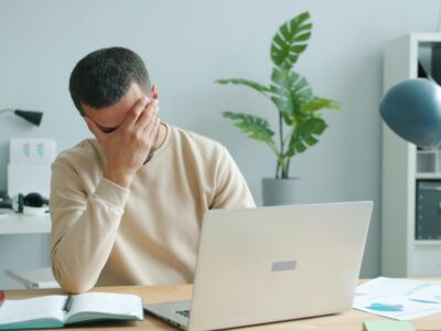 stressed man rubbing his face in front of laptop